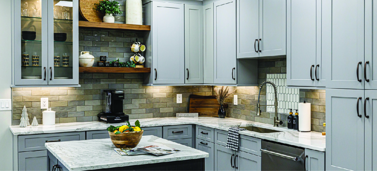 Photo of gray kitchen cabinets with matte black hardware, custom backsplash, and Cambria countertops.